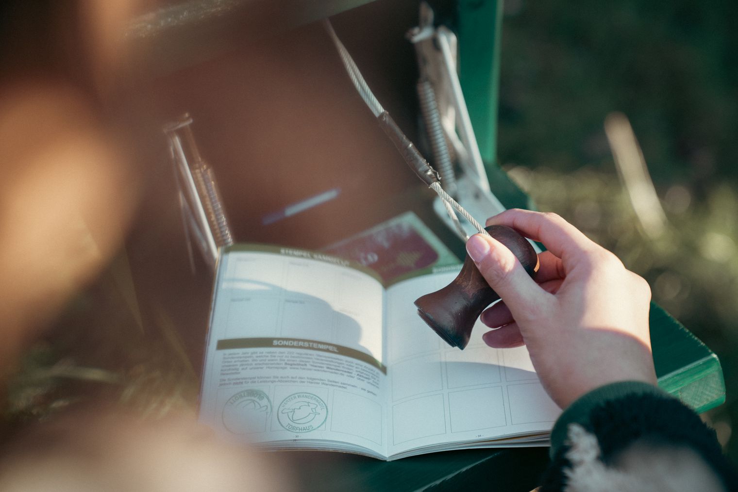 Nahaufnahme einer Hand, die einen Stempel der Harzer Wandernadel in ein geöffnetes Stempelheft drückt.