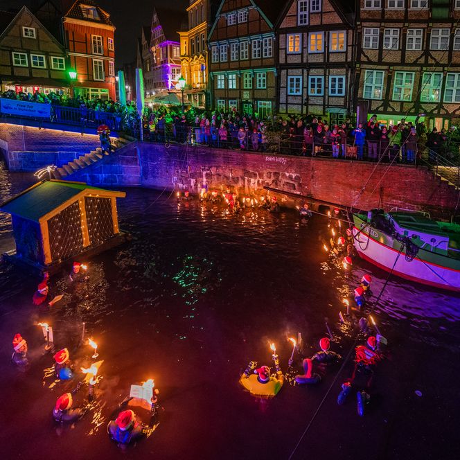 Fackelschwimmer im weihnachtlich beleuchteten Hafen von Stade, umgeben von Fachwerkhäusern und Zuschauern.