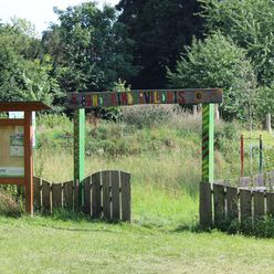 Eingangstor zur Kinderwildnis Nienburg mit üppigem Grün und hölzernem Infobrett im Vordergrund.