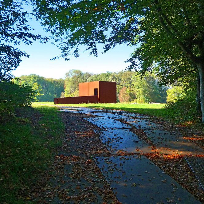 Kunstinstallation aus rostigem Stahl inmitten eines lichten Waldpfades.