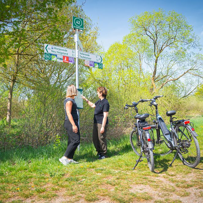 Radfahrerinnen studieren einen Wegweiser mit dem Knotenpunktsystem.