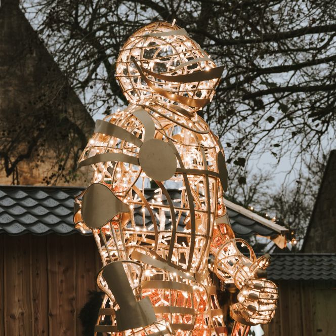 Leuchtende Ritterfigur aus Metall und warmem Licht vor Holzbuden beim Weihnachtszauber Burg Bentheim.