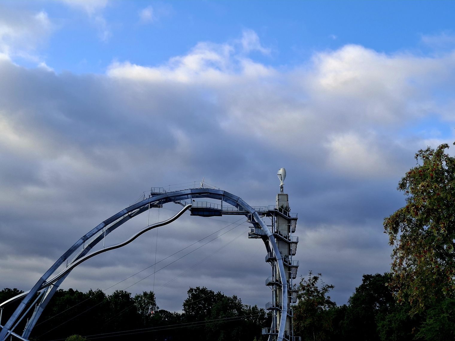 Großer Metallbogen mit Turm und Plattform vor bewölktem Himmel
