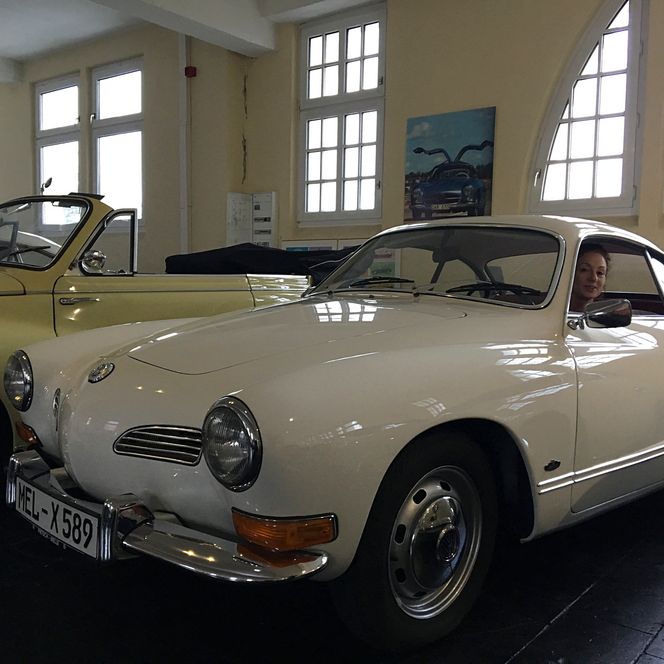 Frau sitzt lächelnd in einem weißen Oldtimer im Automuseum Melle, neben weiteren klassischen Autos.