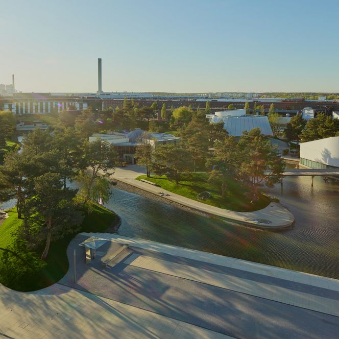 Weitläufige Parklandschaft der Autostadt Wolfsburg mit Wasserflächen, modernen Pavillons und Schornsteinen.