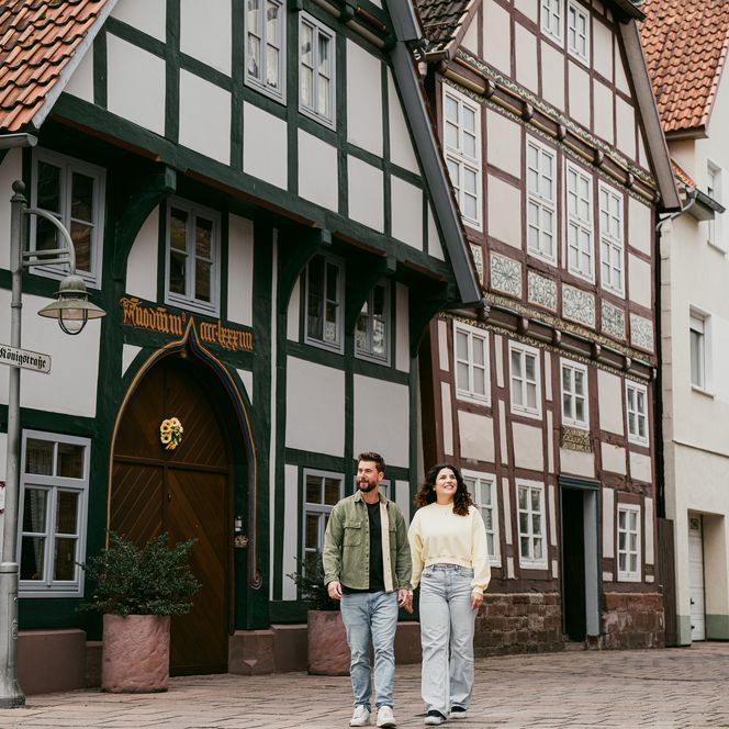 Ein Paar spaziert auf einer Pflasterstraße an historischen Fachwerkhäusern vorbei.