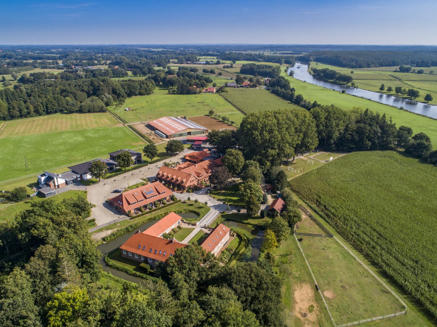 Luftaufnahme von Gut Landegge mit roten Ziegeldächern, Wiesen, Feldern und Fluss im Emsland.