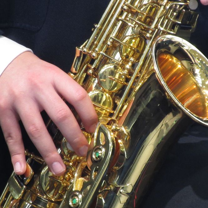 Nahaufnahme eines glänzenden Saxophons in goldener Farbe, das von einer Person in dunkler Kleidung gespielt wird.