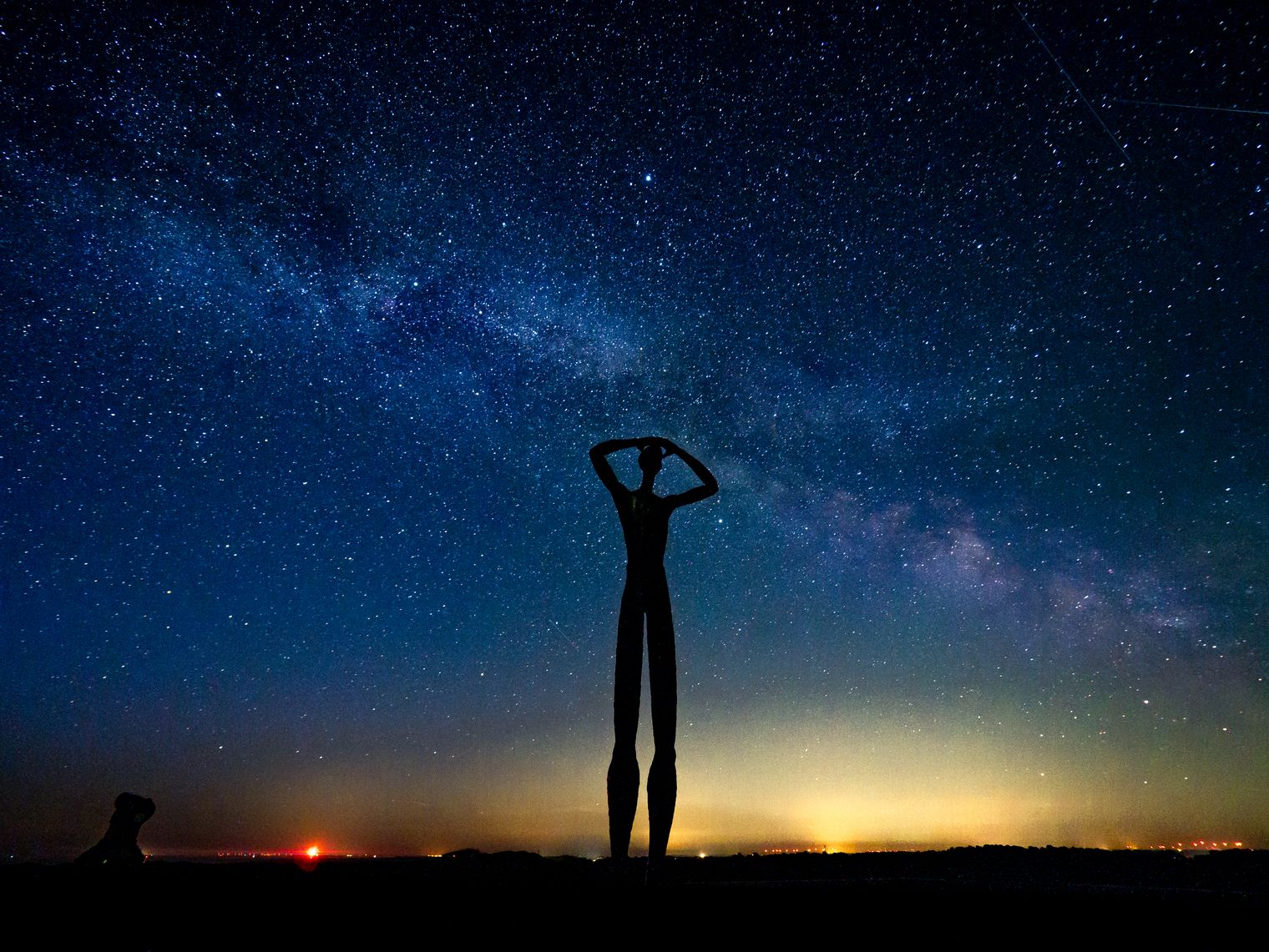 Die Silhouette einer stilisierten Skulptur erhebt sich vor einem Sternenhimmel.