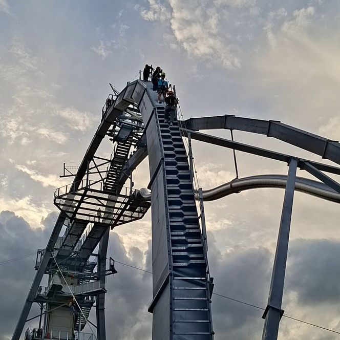 Menschen steigen einen hohen Aussichtsturm vor Abendhimmel hinauf.