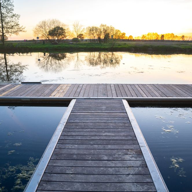 Holzsteg am stillen Wasser im Teufelsmoor bei Sonnenuntergang, umgeben von Bäumen und Spiegelungen.