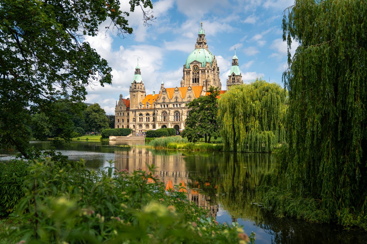 Neues Rathaus Hannover hinter Maschteich, umrahmt von Bäumen und Spiegelung im Wasser.