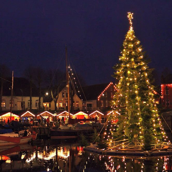 Beleuchteter Weihnachtsbaum im Hafen von Carolinensiel, umgeben von Marktständen und Segelbooten.