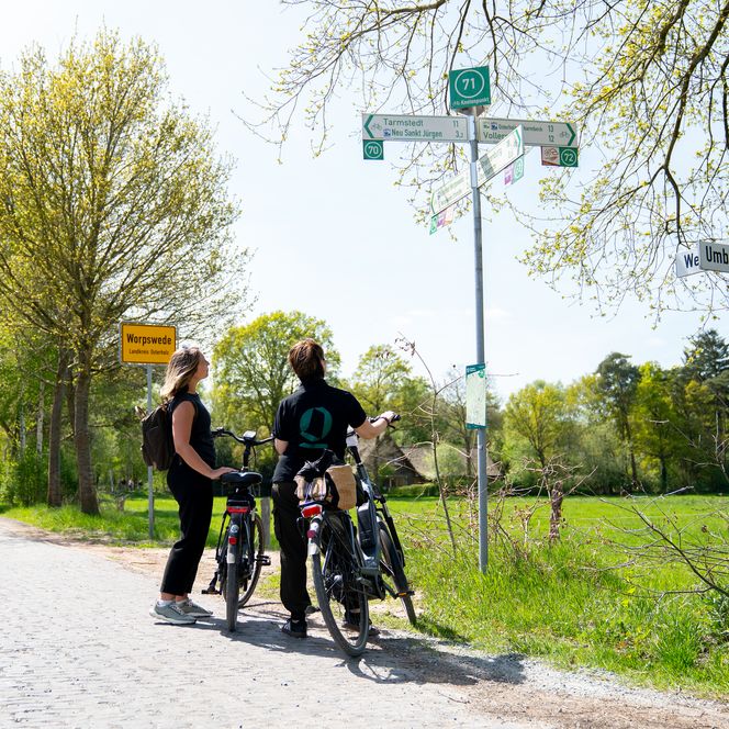 Zwei Radfahrerinnen betrachten einen Wegweiser.