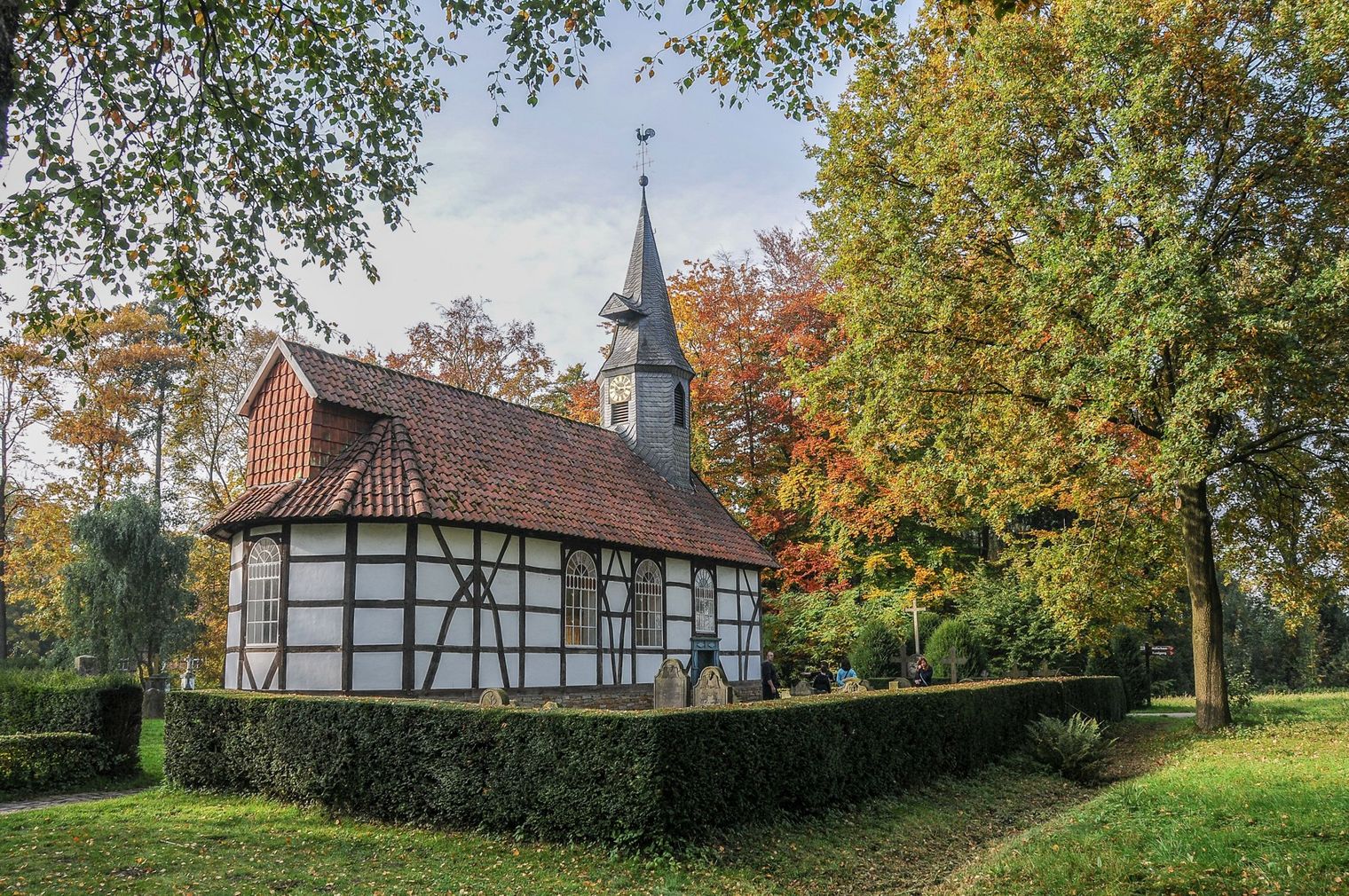 Eine weiß-schwarze Fachwerkkirche mit rotem Ziegeldach inmitten von Bäumen.