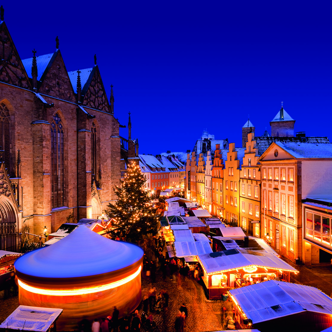 Weihnachtsmarkt in winterlicher Atmosphäre mit hell erleuchteten Ständen und einer historischen Kirche.