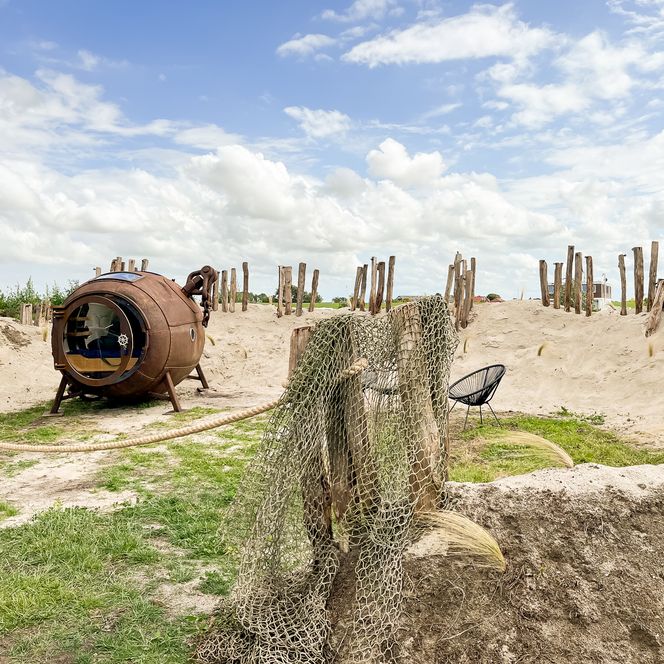 Een slapende boei in het zand met houten palen en visnet onder een blauwe hemel.