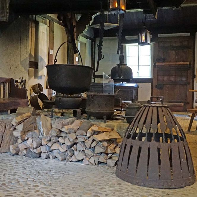 Historische Feuerstelle mit Kochkesseln in einer Bauernstube mit Steinboden und alten Holzmöbeln.