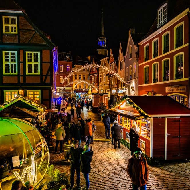 Menschen bummeln über den festlich beleuchteten Weihnachtsmarkt auf dem Stader Fischmarkt.