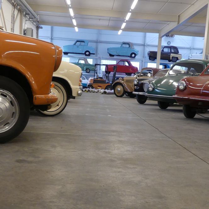 Eine Sammlung bunter Kleinwagen in einer Halle. Viele der Oldtimer sind in Regalen gestapelt.