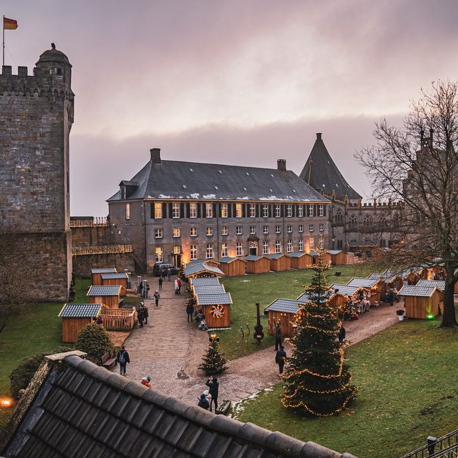 Weihnachtsmarkt in der Burg Bentheim mit Holzbuden, Lichterketten und festlich geschmückten Tannen.