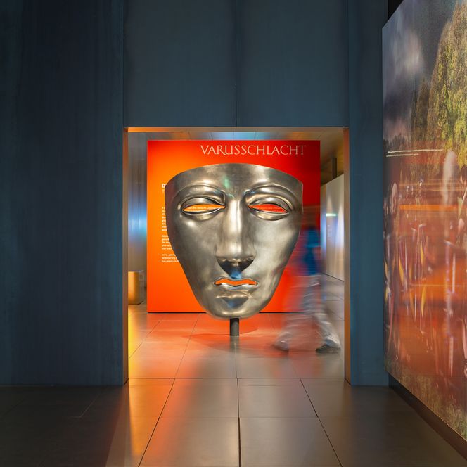 Große silberne Maske im Varusschlacht-Museum mit Besucher im Flur.