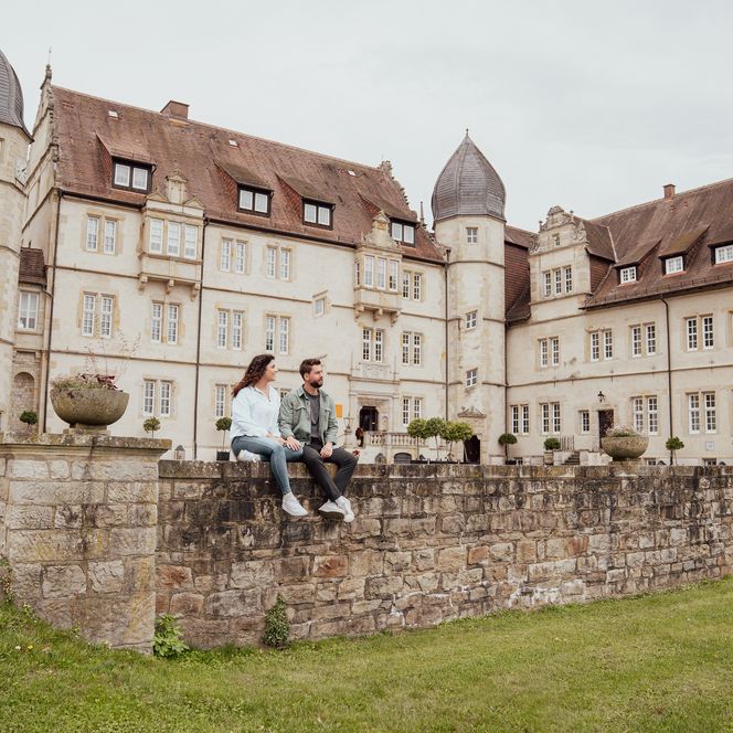 Ein Paar sitzt auf einer Steinmauer vor dem historischen Schlosshotel Münchhausen.