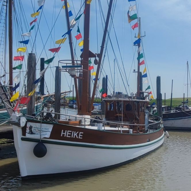 Traditionelles Holzfischereiboot mit bunten Flaggen im Hafen von Jemgum unter blauem Himmel.