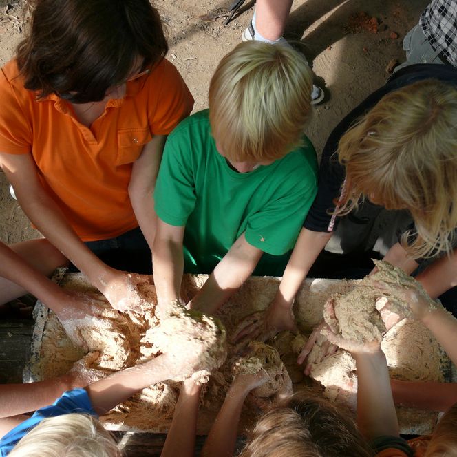 Kinder kneten gemeinsam Brotteig in einer großen Holzwanne.