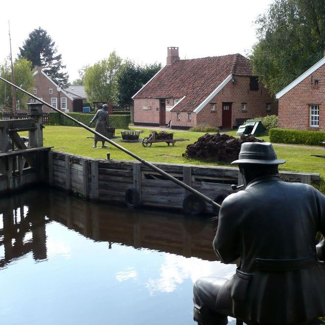 Historische Moorlandschaft mit Backsteinhäusern, Holzschleuse und Bronzefiguren am Wasser in Papenburg