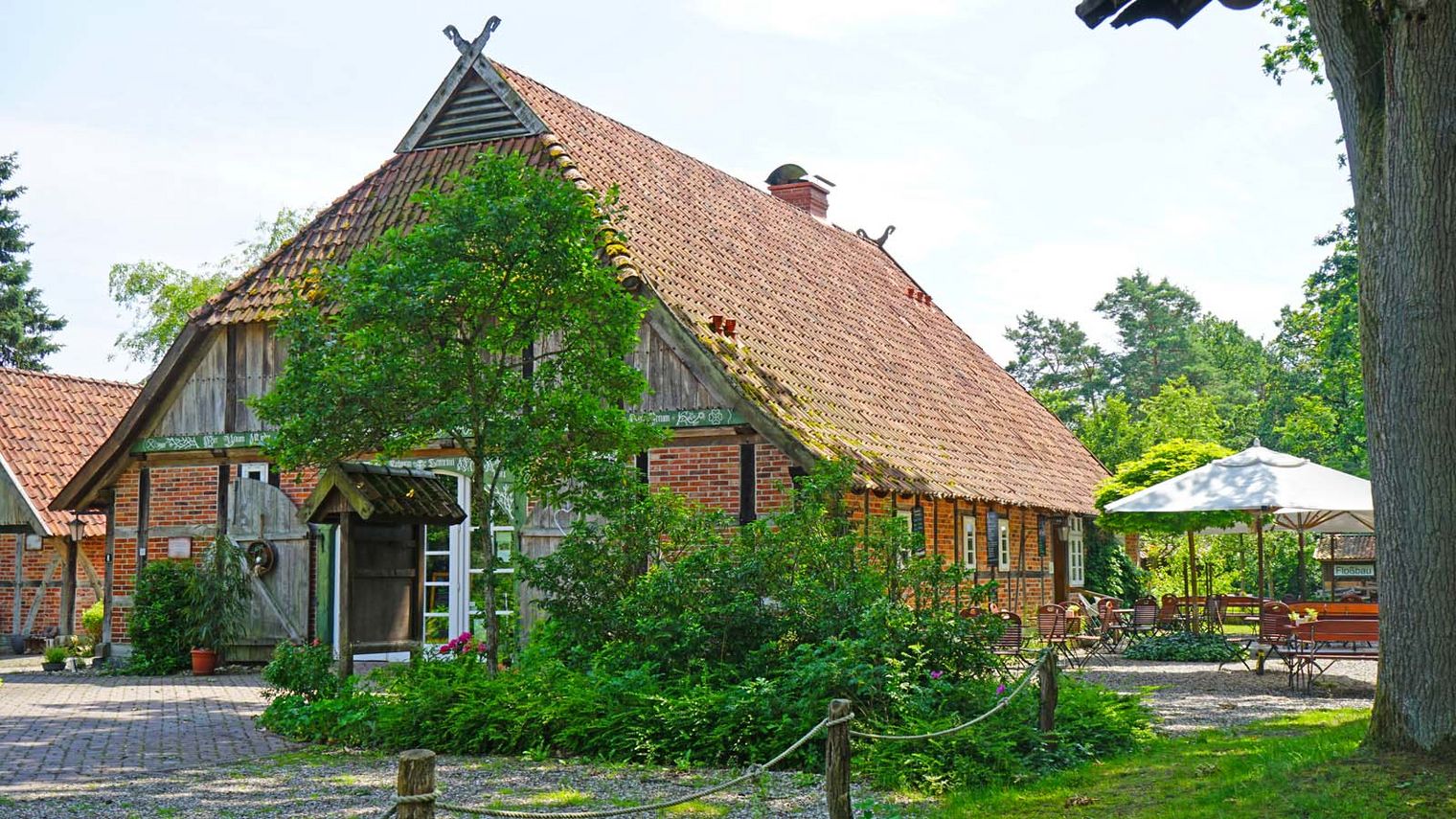 Fachwerkhaus der Kalandstube mit Ziegeldach und Außenbereich mit Bestuhlung unter Bäumen.