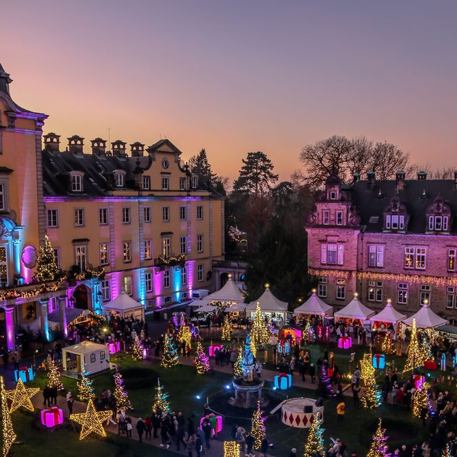 Festlich geschmückter Schlosshof in Bückeburg mit Lichterglanz und Weihnachtsmarktständen bei Dämmerung.