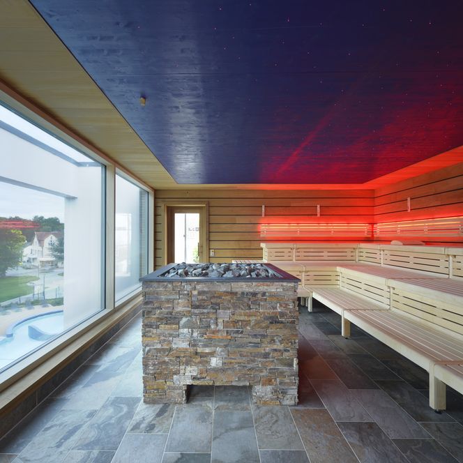 Moderne sauna met panoramische ramen, houten banken en sfeervolle LED-verlichting.