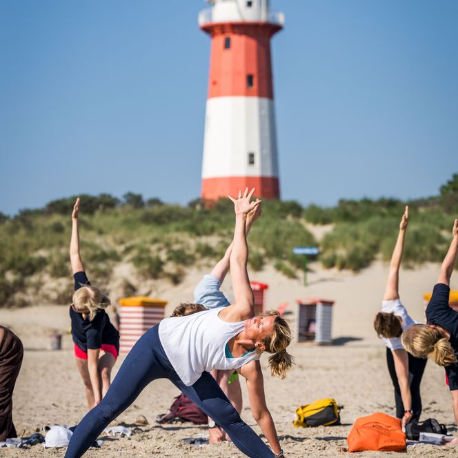 Gruppe macht vor Leuchtturm Yoga am Strand