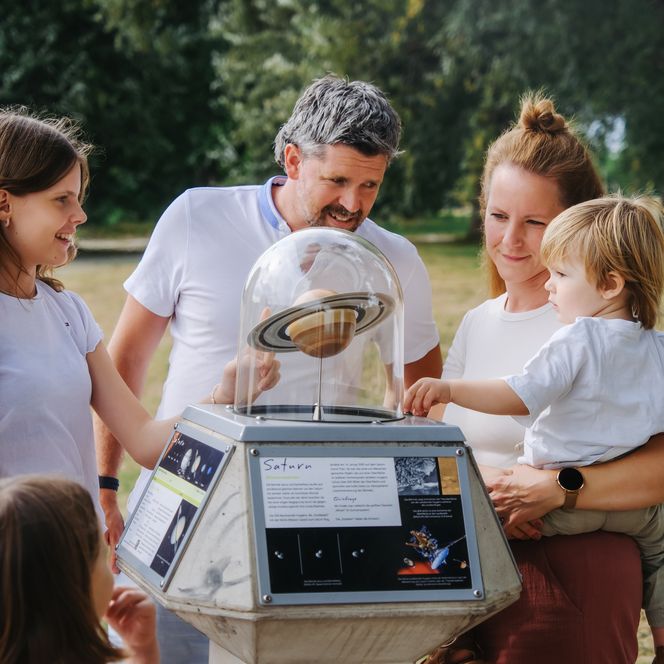 Familie betrachtet ein Saturn-Modell am Planetenweg in Wolfsburg.