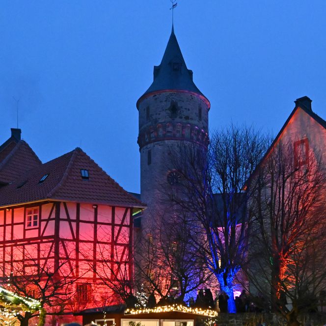 Beleuchtetes Schloss Oelber mit Fachwerkhaus und Turm bei Abenddämmerung während des Christkindlmarktes.