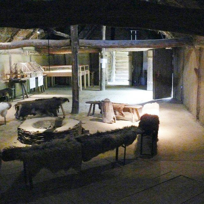 Rekonstruierter Innenraum eines Langhauses mit Feuerstelle, Fellen und Holzbalken im Freilichtmuseum.