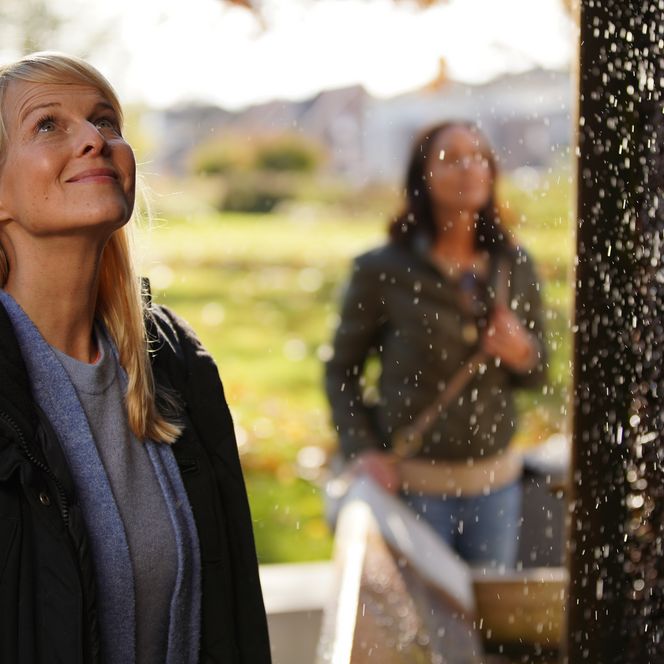 Twee vrouwen zijn gefascineerd door een glinsterende waterval in de buitenlucht.