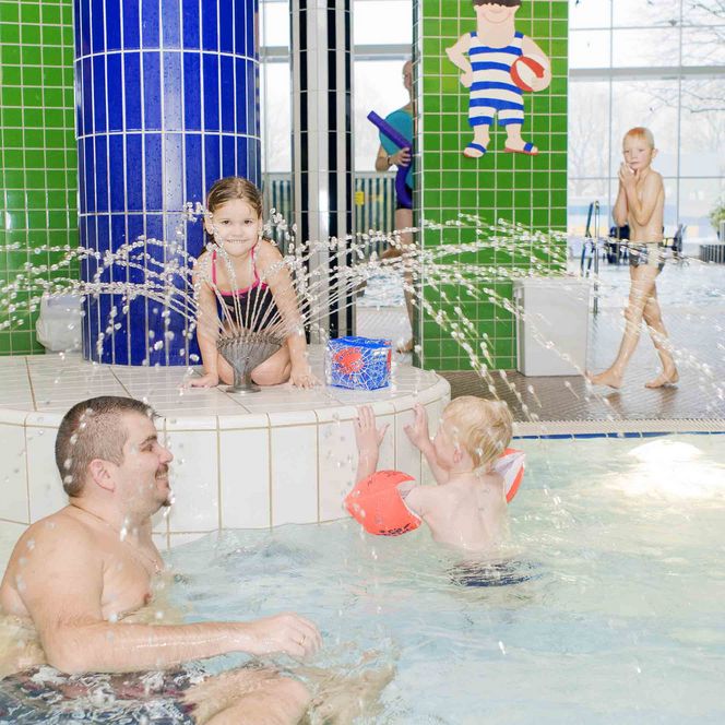 Kinder planschen fröhlich im warmen Hallenbecken mit Wasserfontänen in den Linus Lingen Wasserwelten.