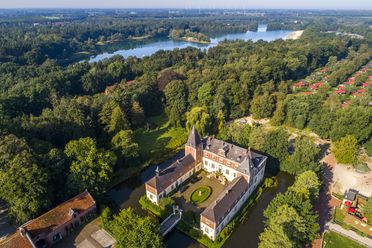 Luftaufnahme von Schloss Dankern mit Wassergraben, See, Waldlandschaft und roten Ferienhäusern.