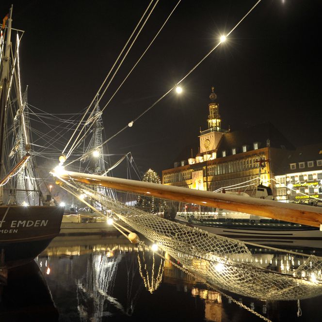 Beleuchtete Segelschiffe am Ratsdelft in Emden vor dem festlich erstrahlten Rathaus bei Nacht.