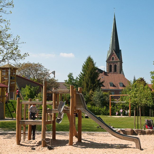 Spielgeräte auf einem Spielplatz. Im Hintergrund ist eine Kirche zu sehen, © LWT / Richard Heskamp