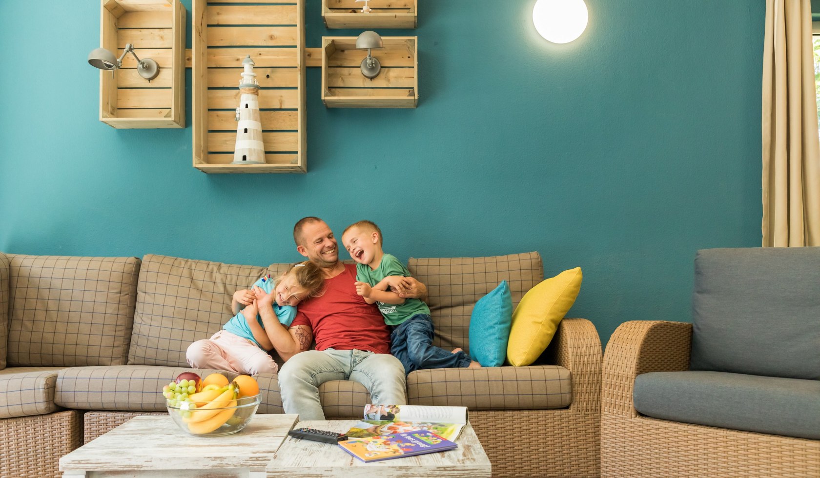 Vater umarmt seine zwei Kindern auf dem Sofa im Ferienhaus., © Center Parcs