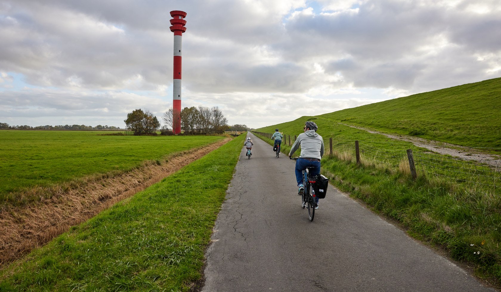 Fahrradfahrer von hinten vor Leuchtturm am Deich , © TourismusMarketing Niedersachsen GmbH