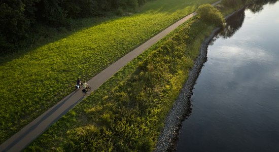 Zwei Radfahrer neben einem Fluss im Weserbergland bei Sonnenstrahlen, © TourismusMarketing Niedersachsen GmbH