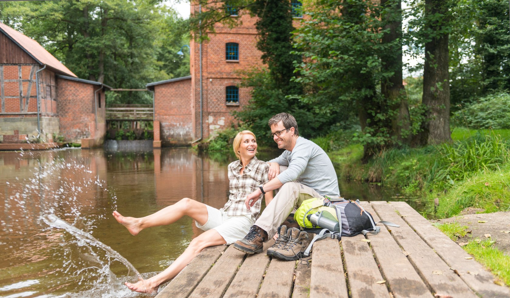 Paar macht eine Wanderpause an der Mühle in Müden und sitzt am Steg, © Lüneburger Heide GmbH / Dominik Ketz