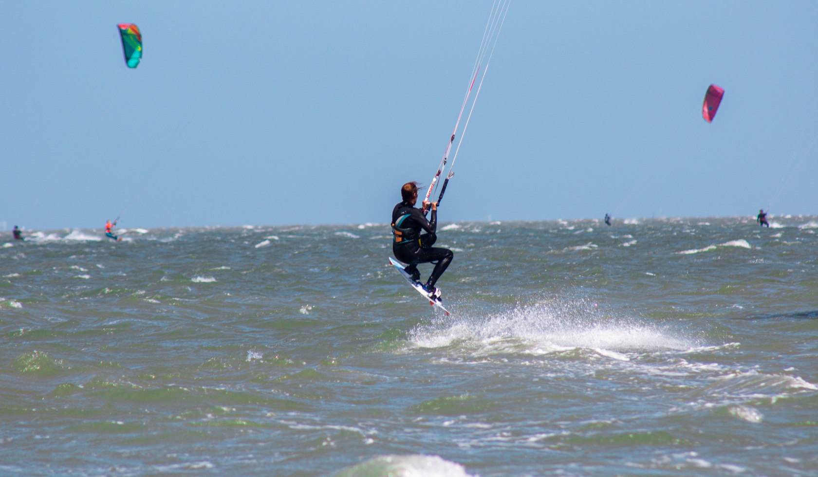 Kiterin im Sprung auf dem Wasser. Im Hintergrund zwei Kitebars am Himmel., © Yara | Unsplash