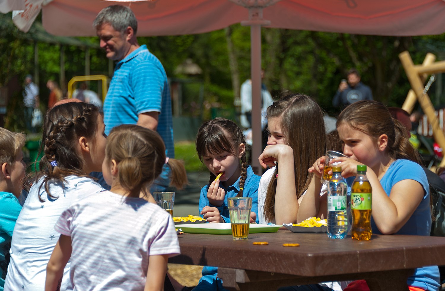 Mehrere Kinder machen Pause im Zoo. Sitzen an einem Holztisch und essen Pommes und trinken Apfelschorle., © Tourismus GmbH Wingst/Bernd Otten