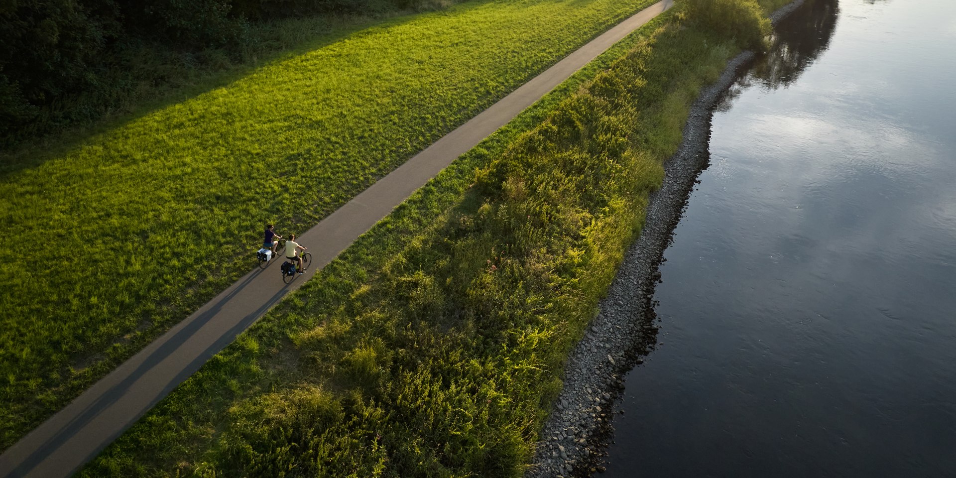 Zwei Radfahrer neben einem Fluss im Weserbergland bei Sonnenstrahlen, © TourismusMarketing Niedersachsen GmbH