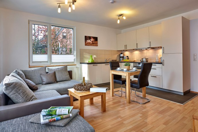 Einblick in den Wohnbereich mit grauem Sofa, kleinem Esstisch und Küche, © Tierpark Nordhorn gGmbH / Franz Frieling